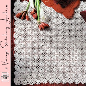 May include: A white rectangular crochet tablecloth featuring a repeating floral motif pattern with a scalloped edge. The textile is displayed over a deep red fabric surface, accompanied by a cluster of red amaryllis flowers. Text reads Vintage Stitchery Archives.
