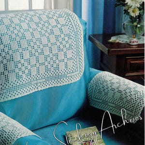 Op de afbeelding: Een witte gehaakte stoelhoes met een geometrisch patroon. De hoes is op een tealblauwe fauteuil met een boek en een bril op de zitting. De tekst "Vintage Stitchery Archives" staat in de linkerbenedenhoek van de afbeelding.