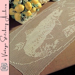 Puede incluir: Camino de mesa de ganchillo de tejido abierto de color crema con un diseño floral central. El camino de mesa es rectangular y presenta un patrón detallado. La imagen también incluye una cesta de limones y el texto "Vintage Stitchery Archives".