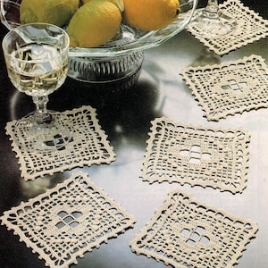 May include: Five crocheted square coasters in a cream colour with a delicate lace pattern. The coasters are arranged on a dark brown surface.