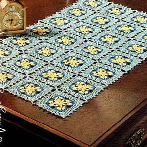 May include: A blue and yellow crocheted table runner with a floral pattern. The runner is on a wooden table.