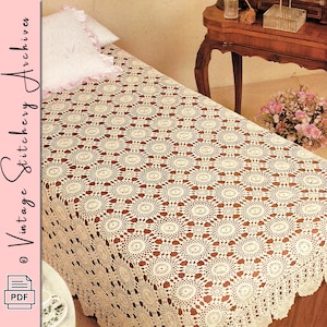May include: An off-white crochet bedspread featuring a repeating circular motif pattern. The textile is draped over a bed, accompanied by a white pillow with ruffled edges. The text Vintage Stitchery Archives is visible on the left side.