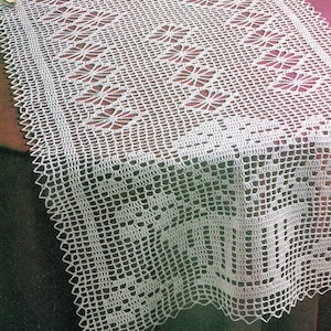 May include: White crocheted table runner with a delicate floral pattern. The runner is made with a fine thread and has a scalloped edge.