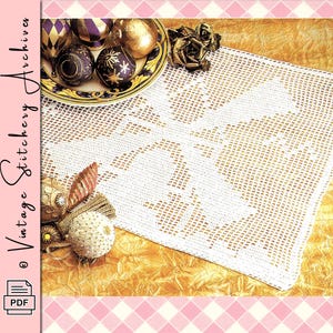 May include: A white, open-weave crochet doily with a floral design. The doily is displayed on a gold-colored, textured surface, with decorative ornaments and a plate of Christmas ornaments. The image also includes the text "Vintage Stitchery Archives" and a PDF icon.