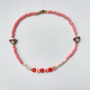 May include: Pink beaded necklace with the name "MINNIE" spelled out in colorful letter beads. The necklace features two Minnie Mouse head charms and gold-colored accents. A charming accessory.