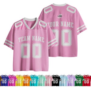 Könnte beinhalten: Rosa Football-Trikot mit weißen Akzenten, mit dem Text "TEAM NAME" und der Nummer "00". Das Trikot hat einen V-Ausschnitt und weiße Streifen auf den Ärmeln. Eine Vielzahl von Trikotfarben wird unten angezeigt.