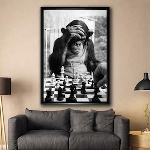 Può includere: Stampa in bianco e nero di uno scimpanzé che gioca a scacchi, con le mani sugli occhi. Una mano umana muove un pezzo sulla scacchiera. La stampa è incorniciata e appesa sopra un divano grigio.