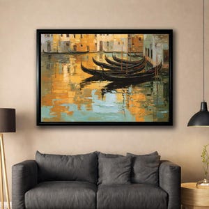 Peut inclure: Peinture encadrée représentant une scène de canal vénitien. Des gondoles sont amarrées dans l'eau, reflétant les tons chauds des bâtiments et du ciel. L'œuvre est encadrée d'un bord noir et est accrochée au-dessus d'un canapé gris.