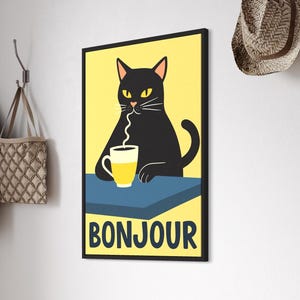 以下が含まれることがあります： 黄色いカップから飲んでいる黒猫が描かれた額入りのアートプリント。下部には「BONJOUR」の文字。猫は黄色の背景に配置されています。壁には麦わら帽子が掛かっています。