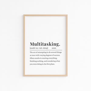 May include: A framed print with the word "Multitasking" in a bold, black font. Below the word is the phonetic pronunciation and the definition of multitasking. The frame is a light brown color.