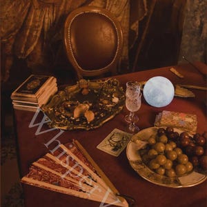 May include: A still life scene with a red table, featuring a decorative fan, a stack of books, a gold-colored tray, a glass, a plate of grapes, and a glowing moon-shaped light. The text "Whisper Veil" is visible.