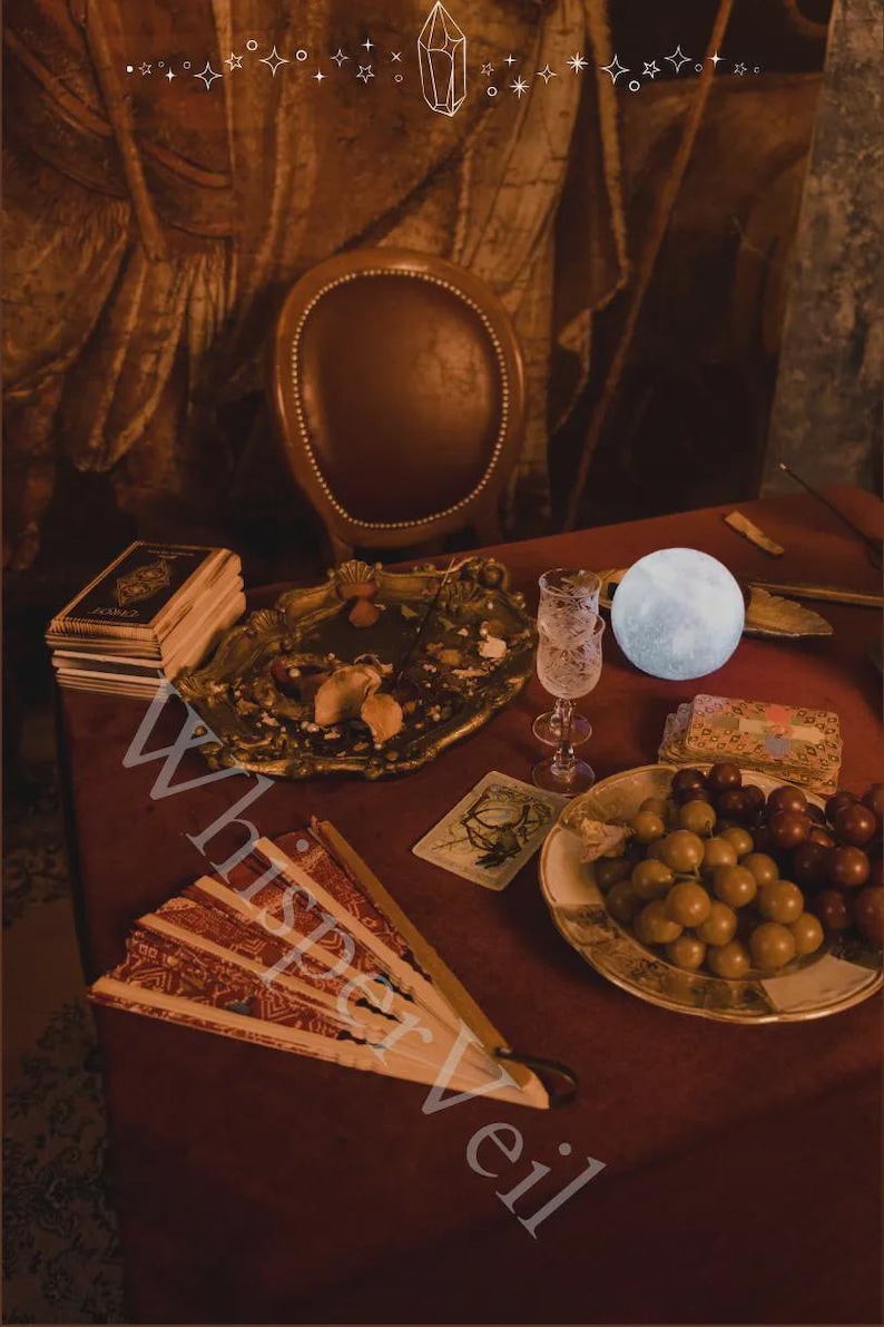 May include: A still life scene with a red table, featuring a decorative fan, a stack of books, a gold-colored tray, a glass, a plate of grapes, and a glowing moon-shaped light. The text "Whisper Veil" is visible.