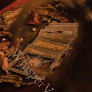 Puede incluir: Un mont&oacute;n de cartas de tarot con ilustraciones coloridas, dispuestas sobre una bandeja decorativa y ornamentada. Las cartas son el foco, con el texto "WhisperVeil" superpuesto. La escena tiene una est&eacute;tica c&aacute;lida y vintage.