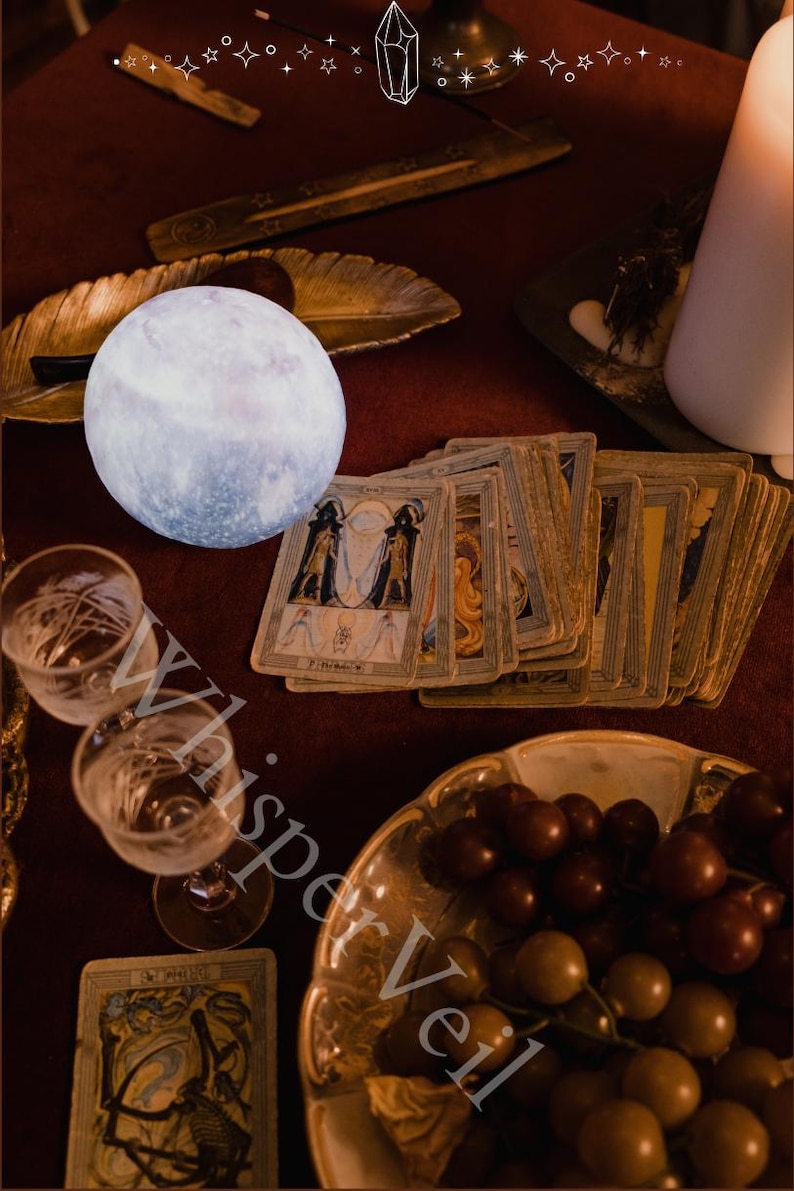 Puede incluir: Una escena m&iacute;stica con una luna brillante, cartas del tarot y una vela encendida sobre una superficie roja. Tambi&eacute;n hay dos copas de vino y un cuenco de uvas. La imagen evoca la adivinaci&oacute;n y las pr&aacute;cticas espirituales.