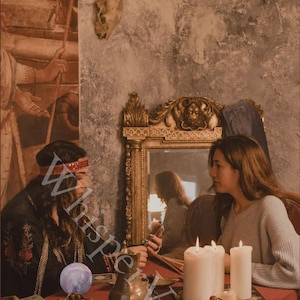 May include: An atmospheric image of two people seated at a table draped in red, engaged in a mystical setting. The scene includes candles, a decorative mirror, and a brass vessel. The word "Whisperveil" is partially visible.