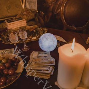 May include: A mystical scene featuring a glowing moon, tarot cards, lit candles, and ornate glassware. A decorative tray holds grapes and other items. The image has a warm, inviting ambiance, with the text "Whisper Veil" visible.