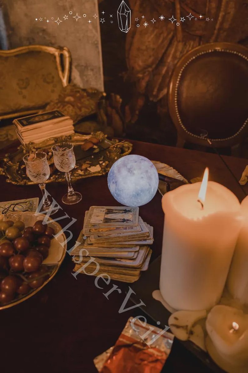 May include: A mystical scene featuring a glowing moon, tarot cards, lit candles, and ornate glassware. A decorative tray holds grapes and other items. The image has a warm, inviting ambiance, with the text "Whisper Veil" visible.