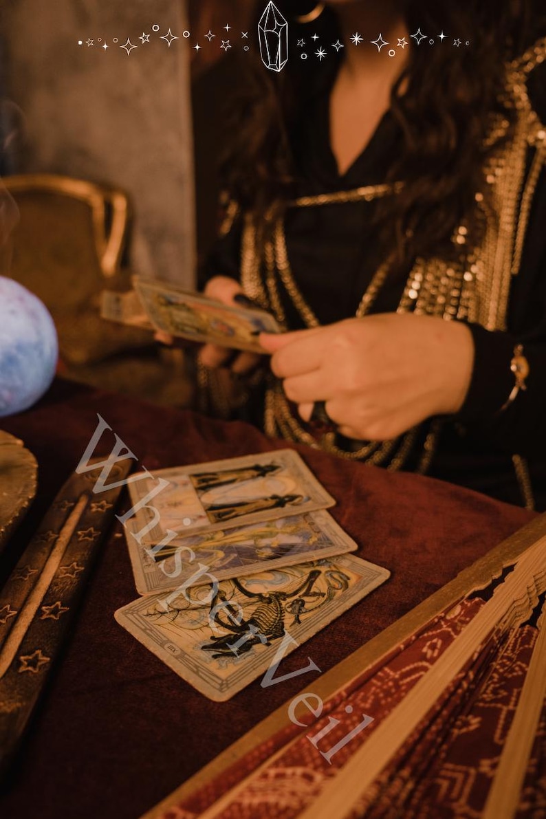 Puede incluir: Cartas del tarot con ilustraciones detalladas dispuestas sobre una superficie de terciopelo burdeos, con una persona sosteniendo m&aacute;s cartas al fondo. Tambi&eacute;n se ven un porta incienso y un abanico decorativo. Tema m&iacute;stico.