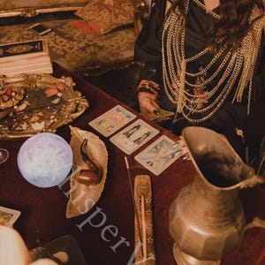 May include: A mystical scene featuring tarot cards, a crystal ball, and an incense holder on a red velvet surface. A decorative metal pitcher and a leather pipe rest on the table. The image has a vintage, bohemian aesthetic.
