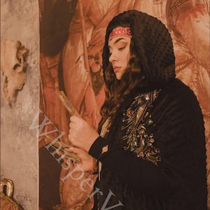 May include: A woman wearing a black hooded cloak with ornate gold and jewel embroidery. She is holding a decorative fan. The background features a Renaissance-style painting with warm tones and the text "Whisper Veil".