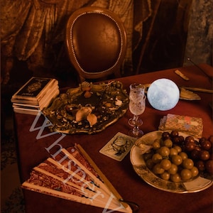 Puede incluir: Un bodeg&oacute;n con una mesa roja, un abanico decorativo, una pila de libros, una bandeja decorativa, una copa, una luz con forma de luna, un plato de uvas y cartas del tarot. El texto "Whisper Veil" es visible.
