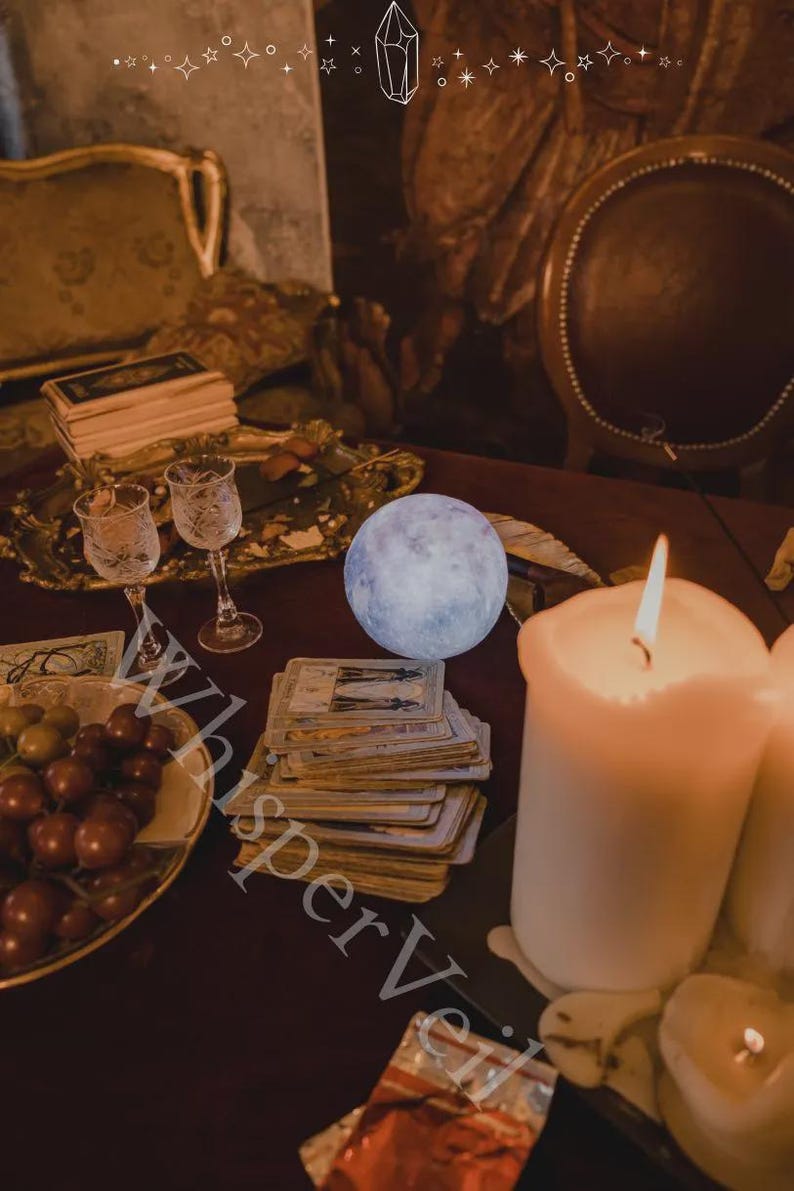 Puede incluir: Una escena m&iacute;stica con una luna brillante, cartas del tarot, velas encendidas y cristaler&iacute;a ornamentada. Una bandeja decorativa contiene uvas y otros objetos. La imagen tiene un ambiente c&aacute;lido, con el texto "Whisper Veil" en la esquina inferior izquierda.