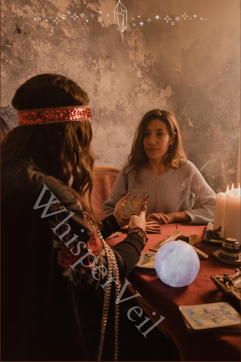 Puede incluir: Una adivina con una diadema roja de lentejuelas y una chaqueta negra con bordados de rosas rojas lee cartas del tarot a una clienta. Un orbe brillante se encuentra sobre una mesa roja, con velas y otros objetos. El texto "Whisper Veil" est&aacute; en la imagen.