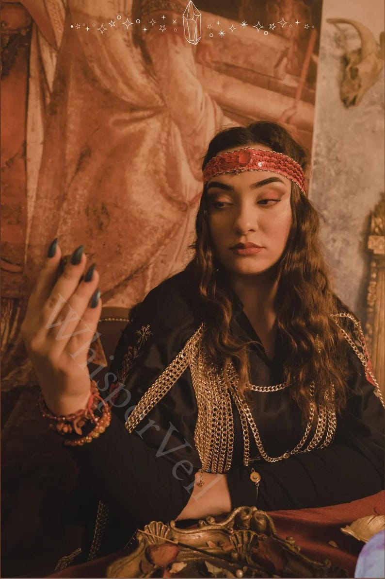 May include: A woman wearing a red sequined headband and a black top adorned with gold chains. The image has a vintage aesthetic, with a warm color palette and a decorative background. The woman is also wearing a red bracelet.