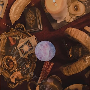 May include: A still-life composition featuring tarot cards, lit candles, and a decorative feather on a dark red surface. A crystal ball and a decorative frame are also present, creating a mystical ambiance. The image has a vintage aesthetic.