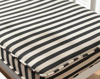 May include: Close-up of a bench cushion with a black and white striped pattern. The cushion has a thick, padded appearance and is bordered with a matching fabric. The bench frame is white.