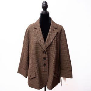 May include: Brown and black checkered blazer with three-quarter sleeves, two front pockets, and three black buttons. The blazer is displayed on a black mannequin against a white background. The jacket has a classic, tailored design.