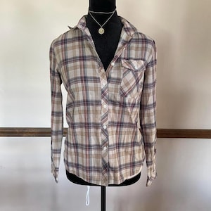 May include: A button-down plaid shirt in beige, burgundy, and navy blue. The long-sleeved shirt has a collared neckline, a single chest pocket, and a classic plaid pattern. The shirt is displayed on a black mannequin.