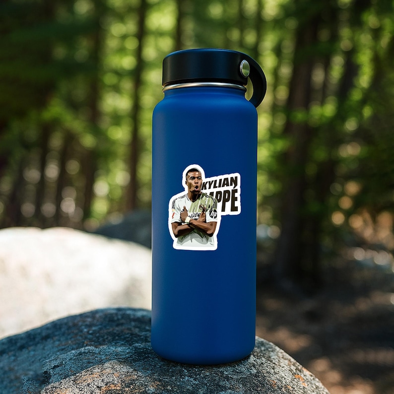 May include: A blue insulated water bottle with a black lid and handle. A sticker of Kylian Mbappe in a white jersey is affixed to the bottle. The sticker has the name "KYLIAN MBAPPE" in white and black.