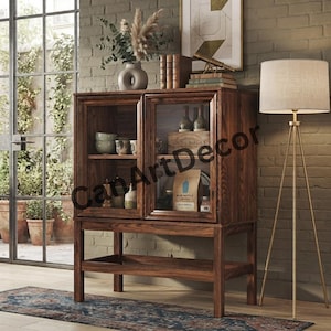 Peut inclure: Une vitrine en bois foncé avec deux portes vitrées, présentant des étagères intérieures contenant des bols en céramique, un sac en papier étiqueté Blue Bottle Coffee et des bouteilles en verre. Le meuble repose sur quatre pieds avec une étagère inférieure et porte le texte CanArtDecor.