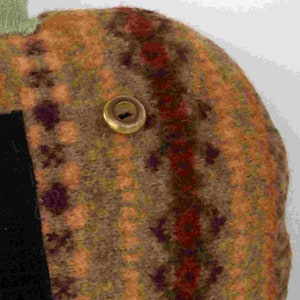 May include: A handmade pumpkin-shaped plush toy with a green stem. The pumpkin is primarily brown with orange and burgundy accents, and a black fabric patch. A gold button is attached.