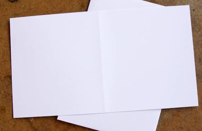 K&ouml;nnte beinhalten: Eine wei&szlig;e, gefaltete Gru&szlig;karte mit leerem Innenraum, die auf einer braunen Oberfl&auml;che liegt. Die Karte ist ge&ouml;ffnet und zeigt einen sauberen, leeren Raum f&uuml;r eine pers&ouml;nliche Nachricht. Das Papier wirkt glatt und knitterfrei.