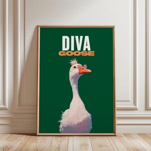 May include: Framed art print showing a white goose with pink sunglasses and a small crown. The words "DIVA GOOSE" are printed in white and orange above the goose on a dark green background. The artwork is in a wooden frame.
