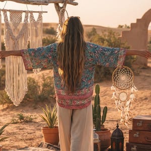 May include: A blue and pink patterned kimono with wide sleeves and loose-fitting beige trousers. The garment features a floral print with a horizontal band of pink and white geometric patterns along the hem and sleeves, worn with light beige pants.