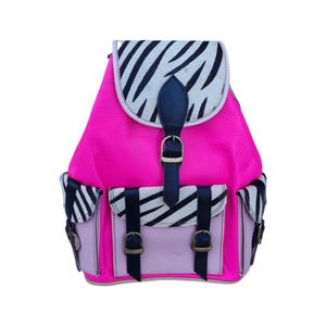 May include: A vibrant pink backpack with a zebra-striped flap and pocket accents. The backpack features a top flap with a dark blue strap and buckle closure, and two front pockets with matching buckles. The bag is made of leather.