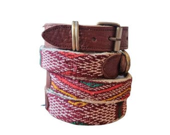 May include: Three belts stacked on top of each other. The top belt is brown leather with a silver buckle. The middle and bottom belts have a woven design with red, white, yellow, and green threads. The belts are for waist sizes.