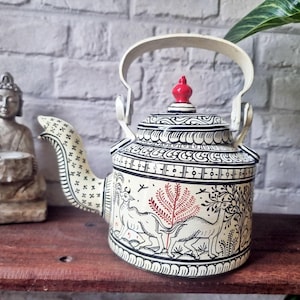 Pode incluir: Bule decorativo creme com detalhes pintados em preto e vermelho. O bule apresenta um bico curvo, uma alça e um botão vermelho. O corpo é adornado com um padrão em preto e branco e ilustrações de animais e árvores.
