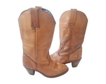 May include: A pair of light brown leather cowboy boots. The boots have a classic design with pointed toes, decorative stitching, and small heels. The boots are made of worn leather.