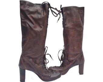 May include: A pair of knee-high brown leather boots with a lace-up design and block heels. The boots have a vintage look and are suitable for various occasions.