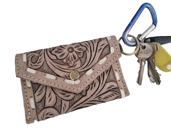 May include: A light brown leather key holder with a floral embossed design and a snap closure. The key holder is attached to a blue carabiner clip with several keys.