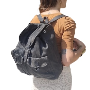 May include: A dark gray backpack with two front pockets and adjustable straps. The backpack has a flap closure and buckle details. The bag is made of a textured material and is worn over the shoulders.