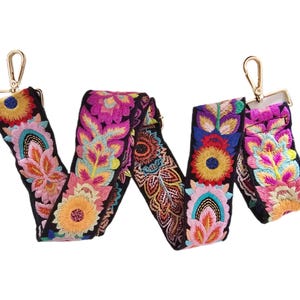 May include: Embroidered bag strap with a floral design in shades of pink, yellow, blue, and orange on a black background. The strap has gold-colored metal clasps on each end.