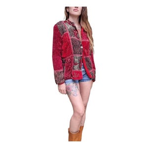 Könnte beinhalten: Rote Patchwork-Jacke mit Samtstruktur und aufwendigen Stickereidetails. Die Jacke hat einen Knopfverschluss und eine kleine Tasche. Das Design integriert verschiedene Muster und Farben und schafft eine Bohème-Ästhetik.