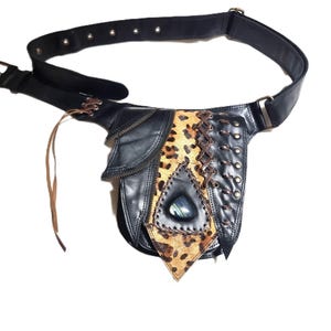May include: Black leather belt bag with leopard print detail and a decorative stone. The bag has a zipped pocket, laced leather features, and a brown leather strap. The belt has a buckle closure.