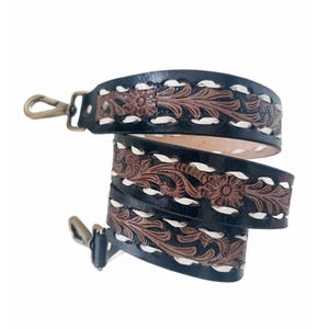 May include: Black leather strap with brown floral tooling and white stitching. The strap has metal swivel clasps on each end. The design features a repeating pattern of flowers and leaves.