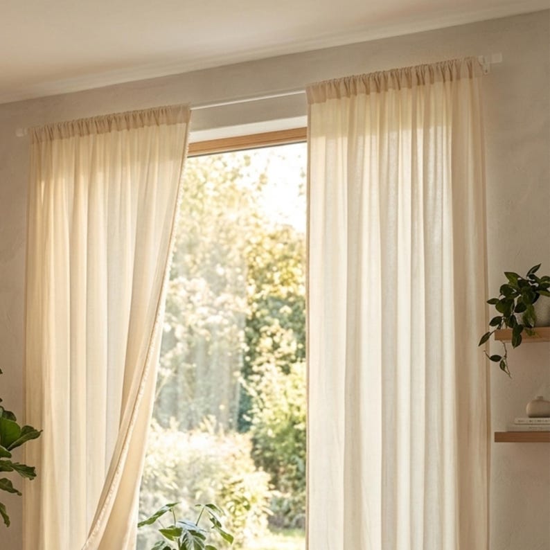 Peut inclure: Des rideaux transparents de couleur cr&egrave;me sont suspendus devant une fen&ecirc;tre, partiellement ouverts pour r&eacute;v&eacute;ler une sc&egrave;ne ext&eacute;rieure ensoleill&eacute;e et lumineuse. Les rideaux sont en tissu l&eacute;ger et sont suspendus &agrave; une simple tringle. La pi&egrave;ce est d&eacute;cor&eacute;e de plantes.
